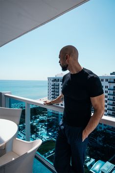 a man standing on top of a balcony next to the ocean and looking out at buildings