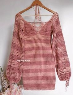 a pink sweater hanging on a wooden hanger next to flowers and a white wall