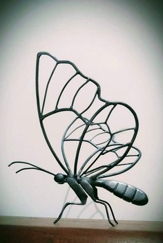 a metal butterfly sculpture sitting on top of a wooden table next to a white wall