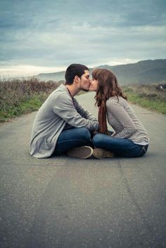 a man and woman sitting on the ground kissing in front of an overcast sky