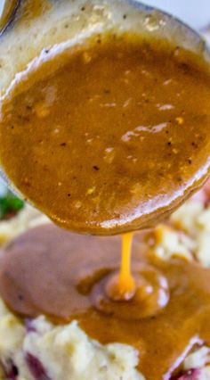 a spoon full of gravy being held over mashed potatoes