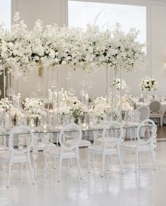 an elegant wedding reception with white flowers and tall centerpieces in the middle of the room