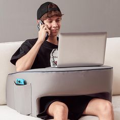 a young man sitting on a couch using a laptop computer and talking on the phone