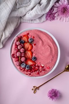 a bowl filled with berries and yogurt on top of a pink surface next to flowers