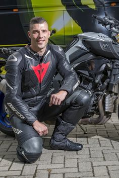 a man sitting on the ground next to a motorcycle wearing a leather suit and boots