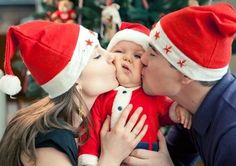 a woman kissing a baby wearing a santa hat