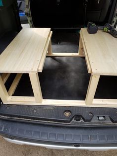 the back end of a van with three tables in it's trunk and one on the floor