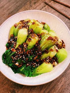 a white bowl filled with green vegetables and sesame seeds on top of a wooden table