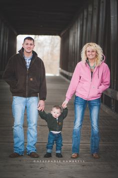 a man, woman and child holding hands while standing on a bridge