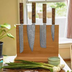 three knives are on a cutting board with green onions