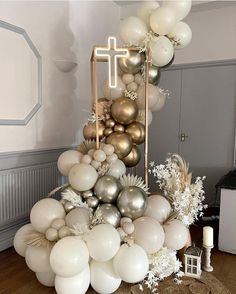 a table topped with white and gold balloons next to a cross on top of a cake