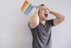 a man is holding a rainbow flag and screaming with his mouth wide open while standing in front of a white wall