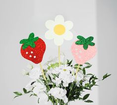 three strawberries and two strawberrys on sticks in a vase filled with white flowers