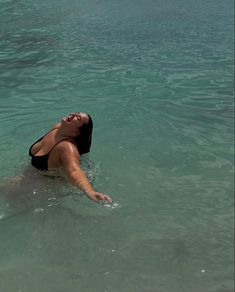 a woman floating in the ocean on top of a body of water with her arms outstretched