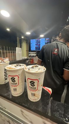 three cups of ice cream sitting on top of a counter next to a man in a black shirt