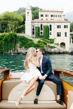 a man and woman sitting on the back of a boat in front of a house