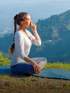 a woman sitting on top of a blue yoga mat while holding a piece of fruit in her mouth