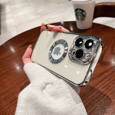 a woman holding up her phone case with the camera lens on it and coffee cup in the background