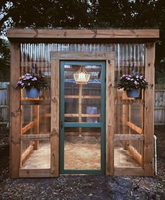 a small wooden structure with two doors and flowers on the top shelf, in front of a fence