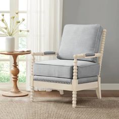 a white chair sitting in front of a window next to a table with a vase on it