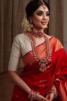 a woman in a red and white sari with pearls on her neck, standing next to a window