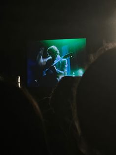 people watching a concert on a large screen in the middle of a dark room with bright green lights