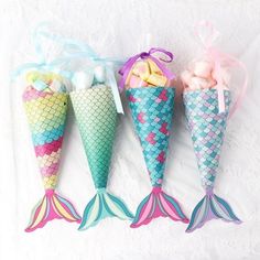 three little mermaid cones with candy in them sitting next to each other on a white surface