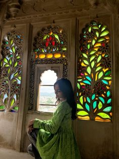 a woman sitting in front of a window with stained glass panels on the windowsill