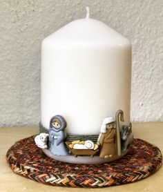 a white candle with nativity scene on it sitting on a table next to a wall