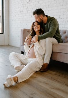 a pregnant woman sitting on top of a couch next to a man who is holding her