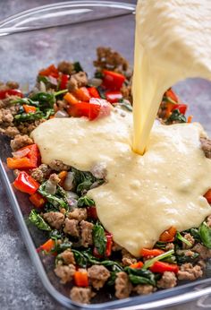 someone pouring cheese on top of some food in a glass dish with spinach and other vegetables