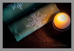 two napkins with white snowflakes on them next to a lit up candle