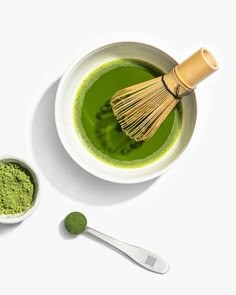 a whisk in a white bowl next to a green powder and a spoon