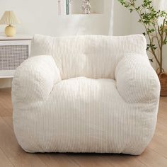 a white chair sitting on top of a hard wood floor next to a lamp and potted plant