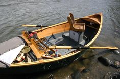 a small wooden boat sitting on top of a river next to rocks and water with an oar sticking out of it's side