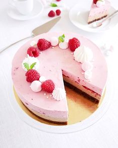 a pink cake with raspberries on top and one slice missing from the cake