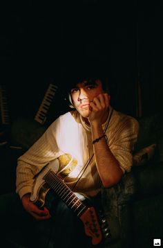 a man sitting on a couch holding a guitar in his hand and looking at the camera