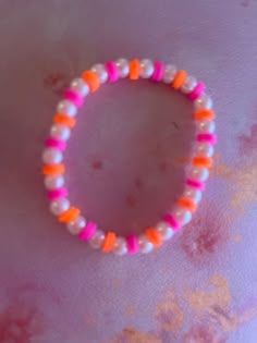 an orange and white beaded bracelet sitting on top of a pink cloth covered table