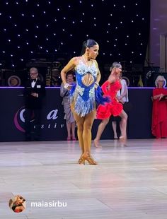 two women in red and blue dresses are dancing on the dance floor with people watching