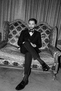 a man in a tuxedo sitting on a couch with his legs crossed and feet crossed