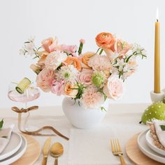 a white vase filled with lots of pink and orange flowers on top of a table