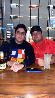 two men sitting at a table with drinks and cell phones in front of their faces