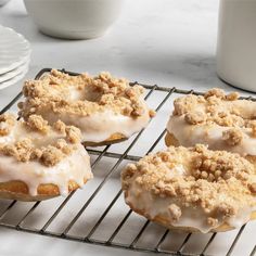 three doughnuts sitting on top of a cooling rack next to plates and cups