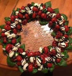 a wreath made out of tomatoes and spinach leaves on a wooden table with white chocolate drizzles