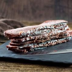 a stack of food sitting on top of a black cutting board next to a knife