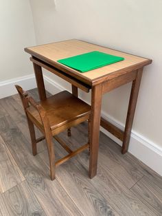 a small wooden table and chair with a green pad on the top, against a white wall