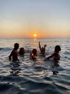 four people in the water at sunset with their arms up and one person reaching for something