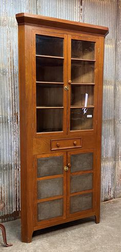 an old wooden cabinet with glass doors on the top and bottom, in front of a corrugated wall