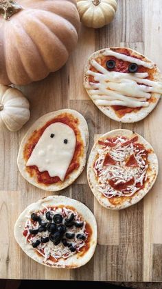 three pizzas with faces on them sitting on a wooden table next to pumpkins