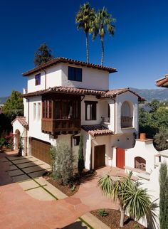 a large white house with palm trees in the front yard and mountains in the background